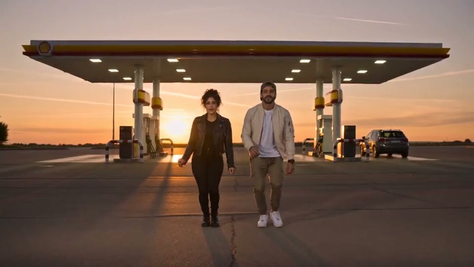 Two people walking in front of a gas station at sunset