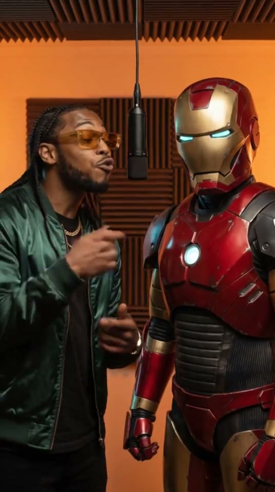 A performer beside a red-and-gold armored character at a studio microphone
